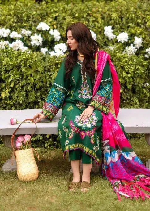 Elegant woman in green winter wedding attire with vibrant accents, holding flowers by a garden bench.